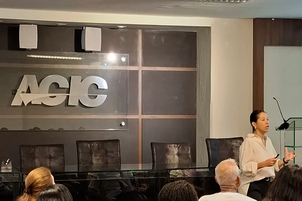 Pessoas sentadas acompanhando uma apresentação no auditório com a identificação ACIC.