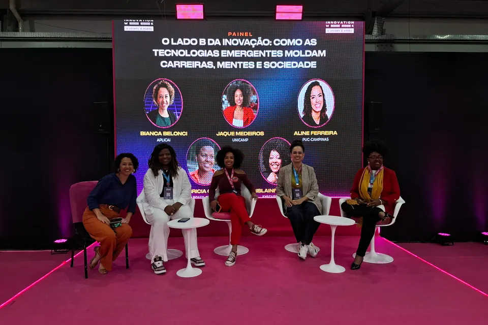 Cinco pessoas sentadas em poltronas no palco diante de um painel.